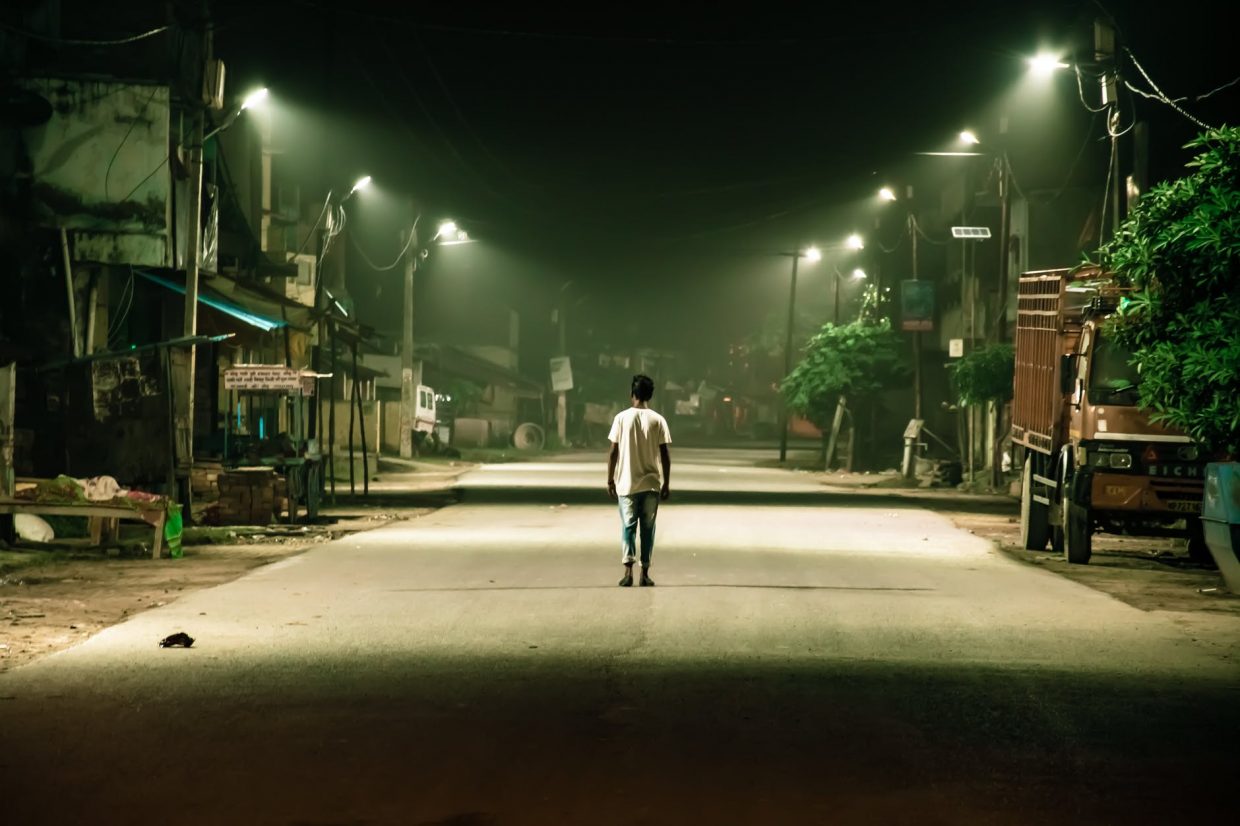 man wearing crew neck t shirt walking on gray pathway during nighttime