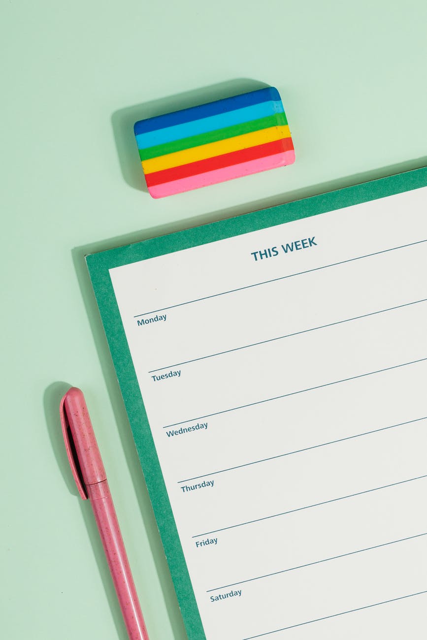 a weekly planner beside a colorful eraser and a yellow pair of scissors